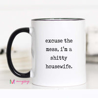 Mug with text 'excuse the mess, i'm a shitty housewife.' on a white background