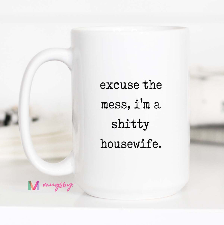 White mug with text 'excuse the mess, i'm a shitty housewife.' on a white background