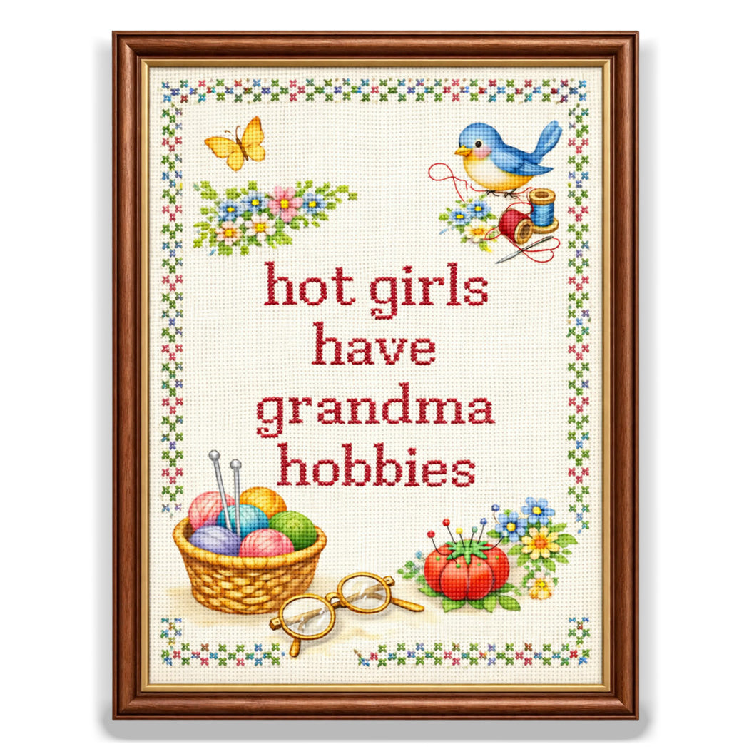 Vinyl sticker designed to look like a framed cross-stitch sampler with the phrase "hot girls have grandma hobbies" surrounded by embroidery-style flowers, a bluebird, yarn, and reading glasses