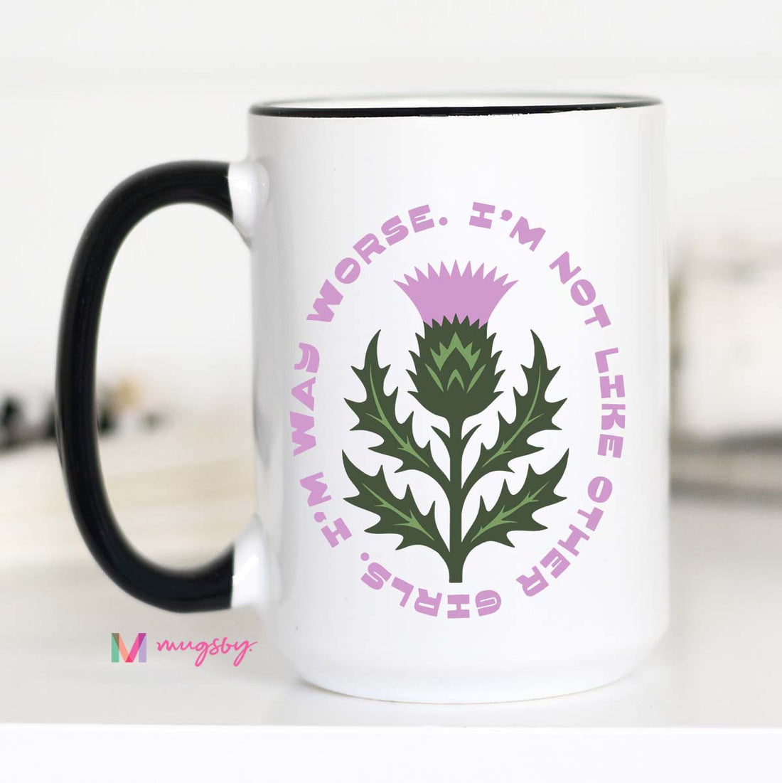White mug with green thistle design and pink text on a white background