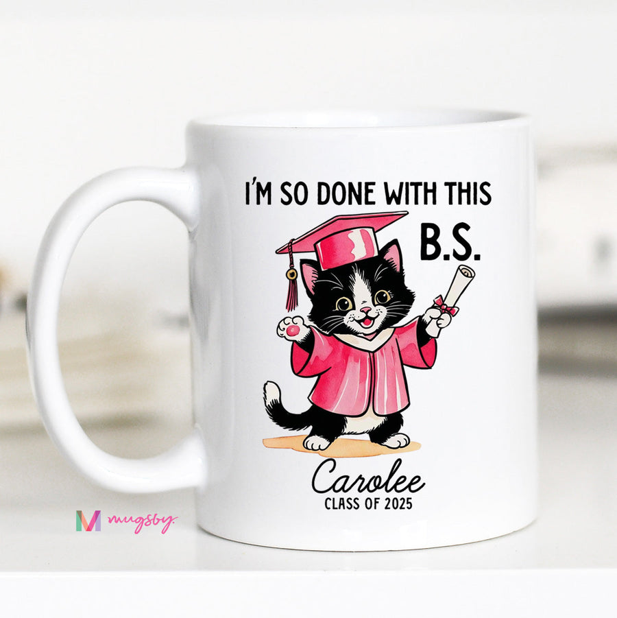 A personalized coffee mug with a cartoon image of a cat wearing a graduation cap and gown, holding a diploma, with the text 'I'M SO DONE WITH THIS B.S.