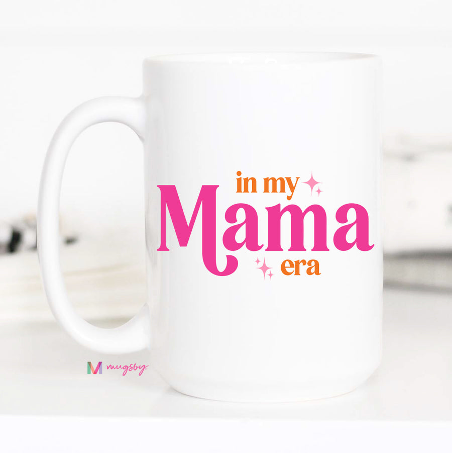White mug with 'in my Mama era' text in pink and orange on a white background