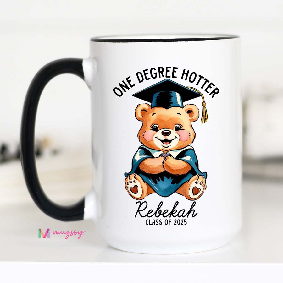 A white ceramic coffee mug with a black handle featuring a cartoon bear wearing a graduation cap and the text 'One Degree Hotter', with a personalized name 'Rebekah' and 'Class of 2021'.
