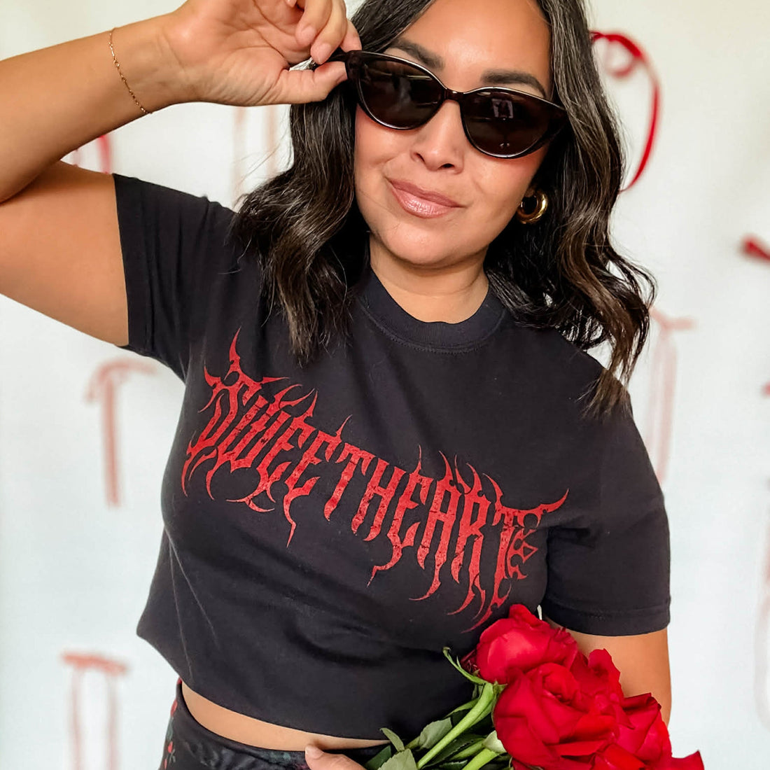 Woman wearing a black t-shirt with red text, holding sunglasses and red roses.