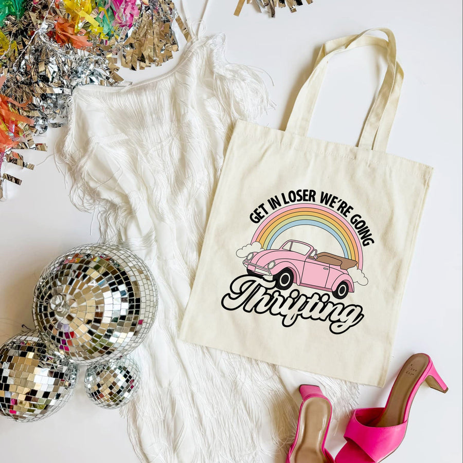 Tote bag with a car and rainbow design, surrounded by disco balls and high heels on a white surface.