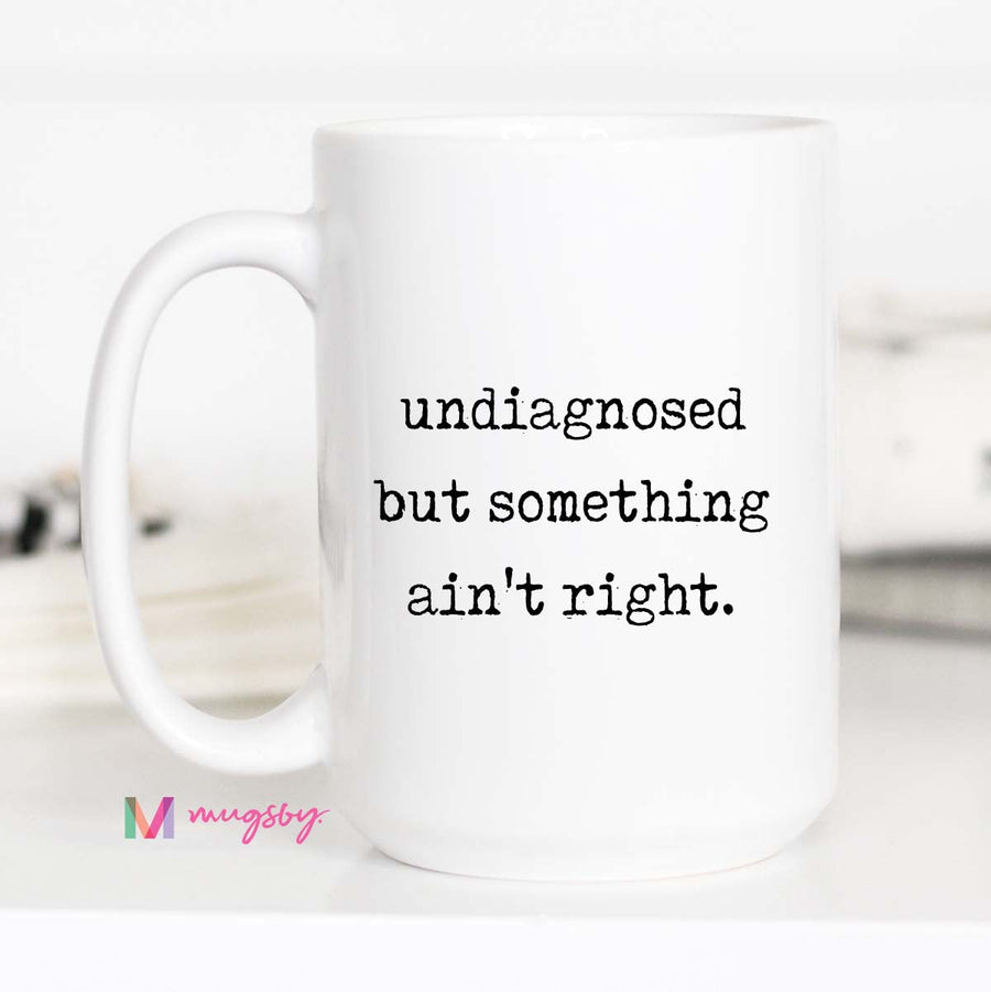 White mug with text 'undiagnosed but something ain't right' on a white background
