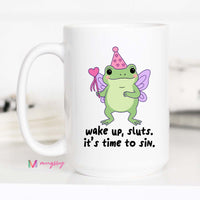 Mug with a fairy frog design and text 'wake up, sluts. it's time to sin.' on a white background.