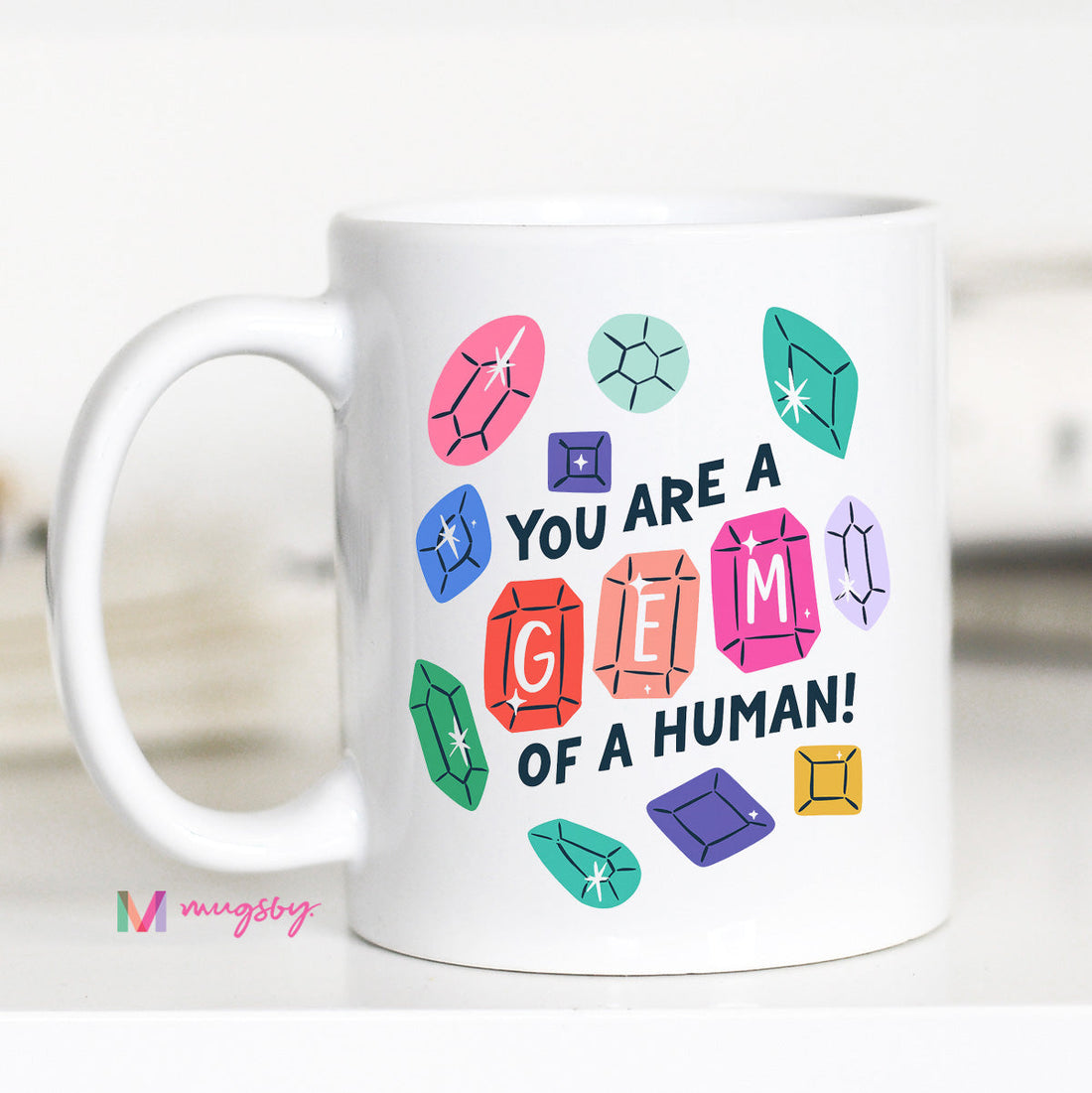 White mug with colorful gemstone designs and text on a white background